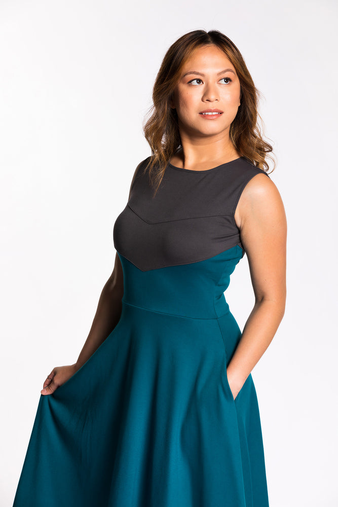 Chelsea is wearing the Fighter Longsword Dress - Teal. Her left hand is in her left skirt pocket. Chelsea is wearing an extra small. Her measurements are 36" Bust, 29" Waist, and 39" Hips, and she is 5'4".