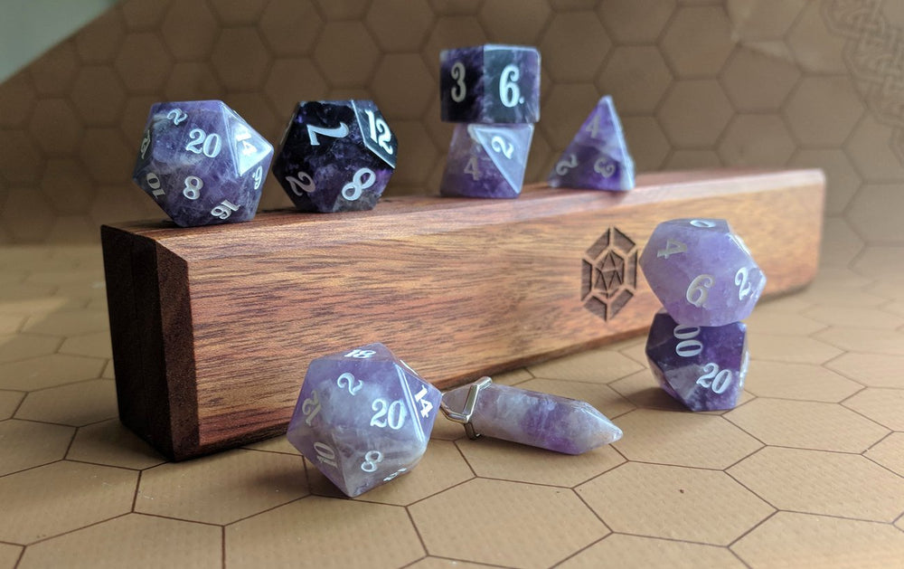 A set of Level Up Dice's amethyst dice and pendant atop a wooden dice vault