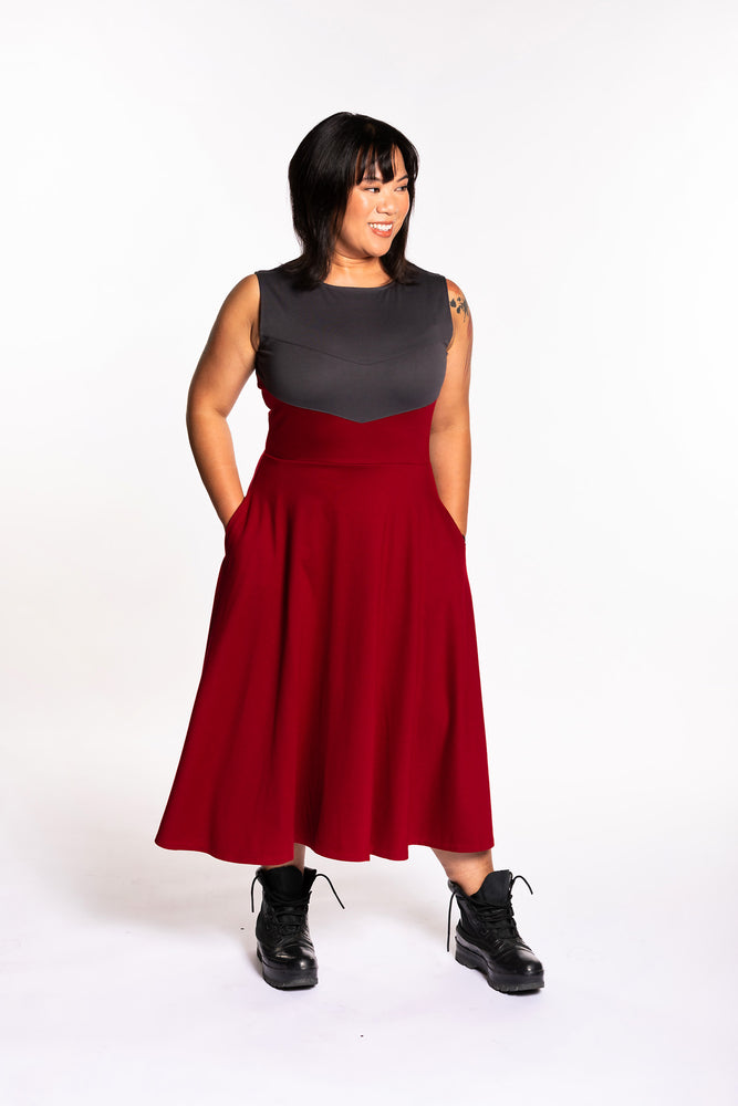 Cheryll is wearing the Fighter Longsword Dress - Ruby. Both hands are in her skirt pockets. She is wearing a medium. Her measurements are a 40" Bust, 32" Waist, and 40" Hips, and she is 5'4.5"