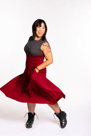 Cheryll is wearing the Fighter Longsword Dress - Ruby. She's twirling her skirt with both hands are in her skirt pockets. She is wearing a medium. Her measurements are a 40" Bust, 32" Waist, and 40" Hips, and she is 5'4.5"