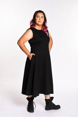Jessica is wearing the Fighter Longsword Dress - Black. Her right hand is placed in the pocket of her skirt. She is wearing an extra large. Her measurements are 47" Bust, 37" Waist, and 46" Hips, and she is 5'6"