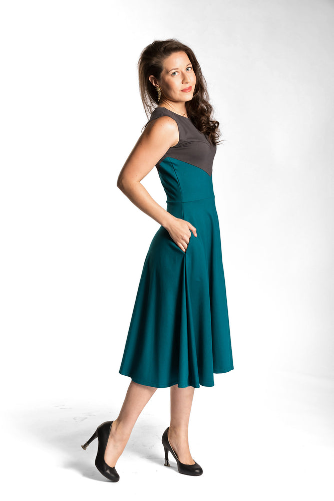 Victoria is wearing the Fighter Longsword Dress - Teal side view. Her right hand is in her right skirt pocket. Victoria is wearing an extra small. Her measurements are 34" Bust, 28" Waist, and 39" Hips, and she is 5'6".